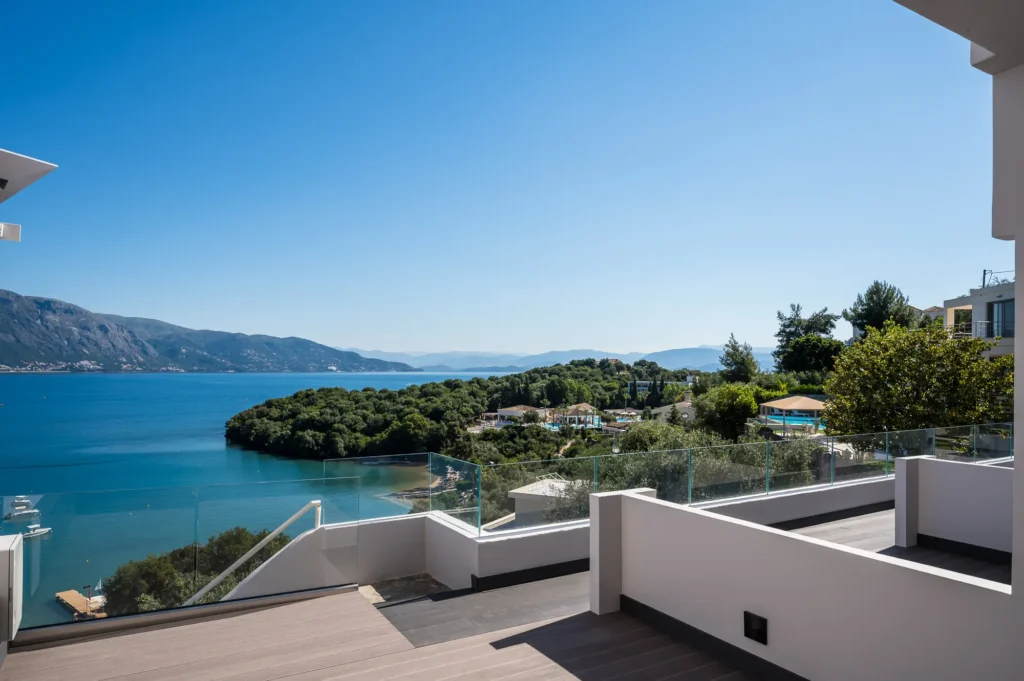 Modern terrace with glass railing looking out over a blue bay and distant hills white walls on the right