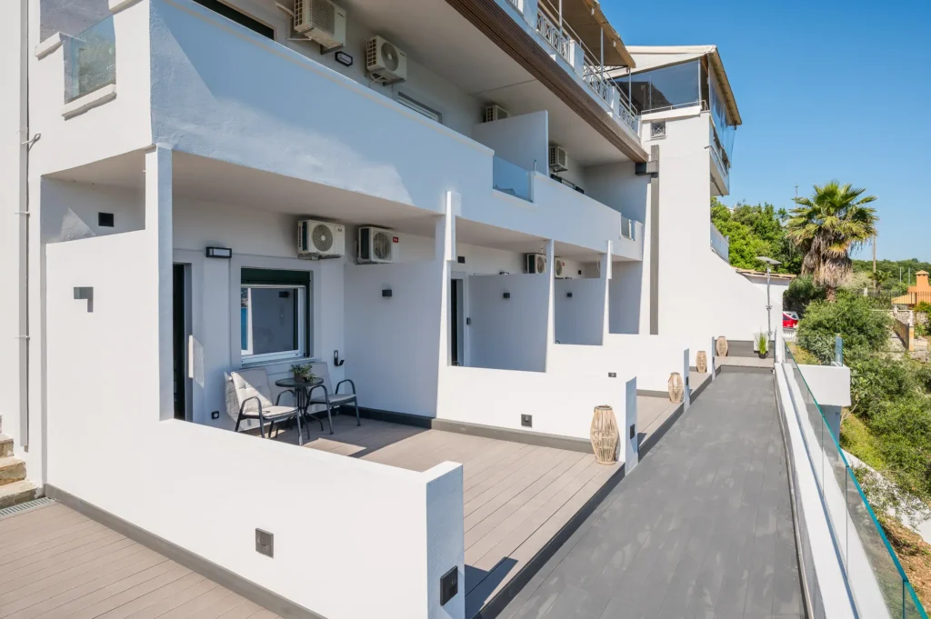 Modern white apartment building with balconies glass railings and outdoor seating on a sunny day