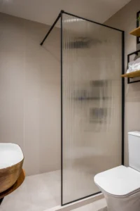 Modern bathroom with a frosted ribbed glass shower screen, beige tiled walls, and a white toilet visible at the edge of the frame.