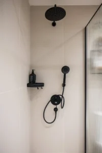 Modern shower with a large circular ceiling rain shower and a handheld shower, black fixtures, and a glass partition on the right.
