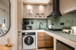 Compact modern kitchen with a front-loading washing machine under the counter and a green backsplash area above the sink