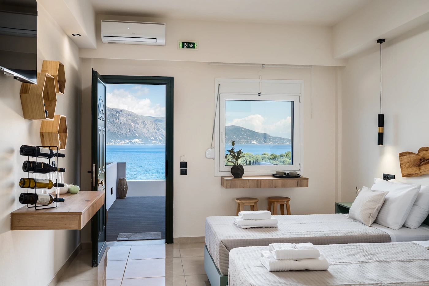 Hotel room with two single beds and white bedding, a wooden headboard, and a view of the ocean through an open balcony door.