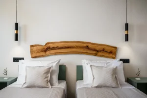 Twin beds in a modern hotel room with a live-edge wood headboard, white bedding, green nightstands, and hanging pendant lights.