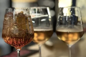 Three stemmed glasses with ice and amber-colored drinks on a bar counter, close-up view.