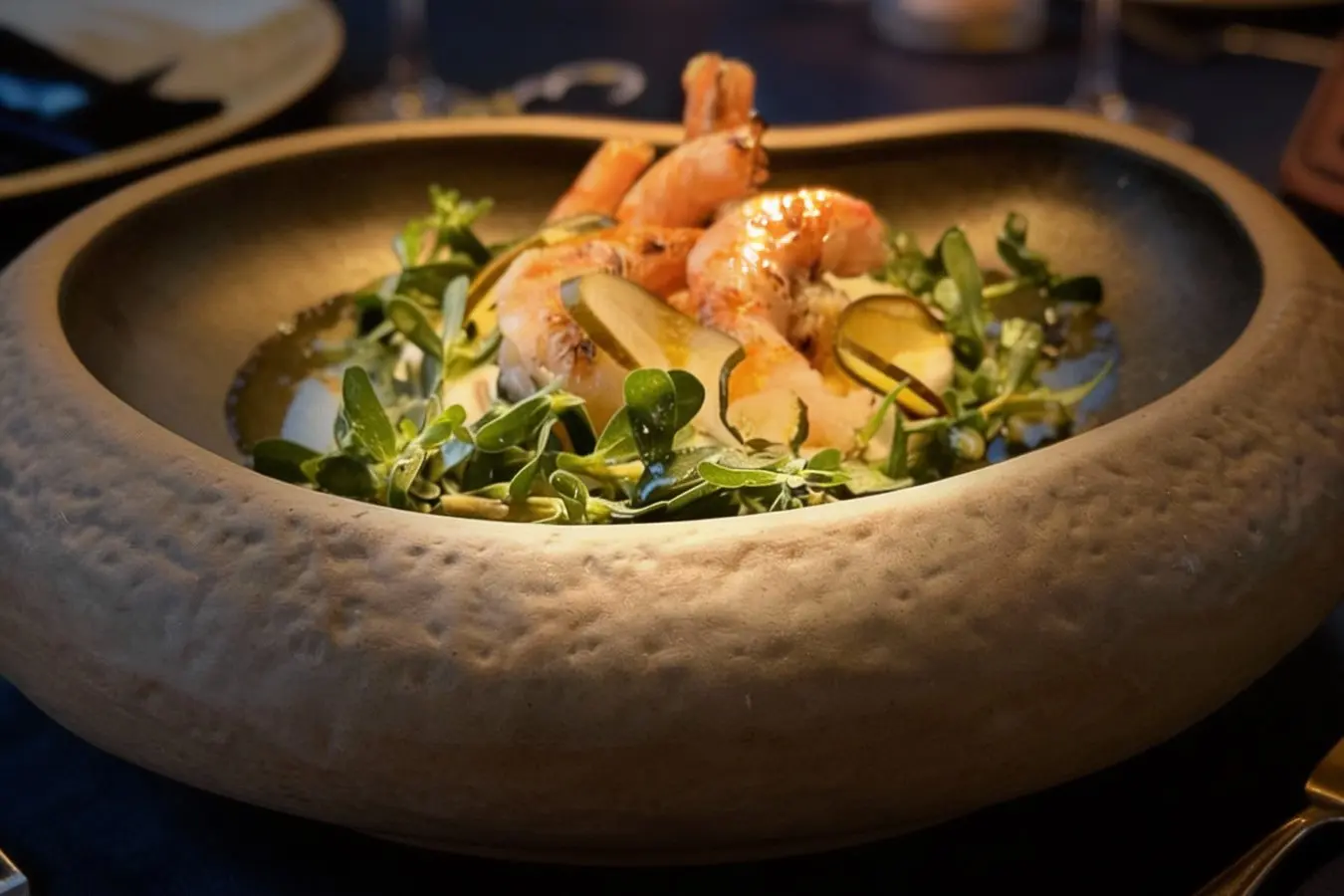 Shrimp dish with greens and lemon wedges served in a round, textured stone bowl