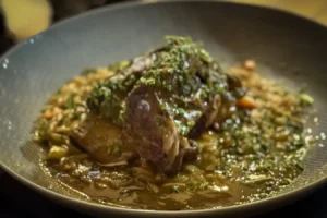 Braised beef short rib with chopped herbs in a rich brown sauce over a bed of mushrooms and grains on a dark plate.