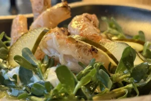 Shrimp atop a bed of fresh greens with lime wedges on a plate, close-up view.